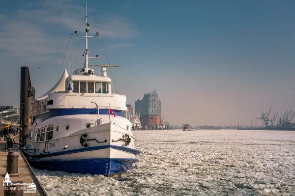 Das ehemalige Fahrgastschiff TONNE im Eis vor den Landungsbrücken mit Elbphilharmonie im Hintergrund.