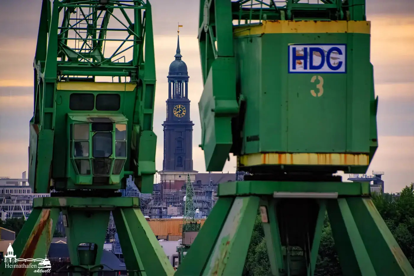 Hamburger Michel zwischen grünen Hafenkränen bei Sonnenuntergang