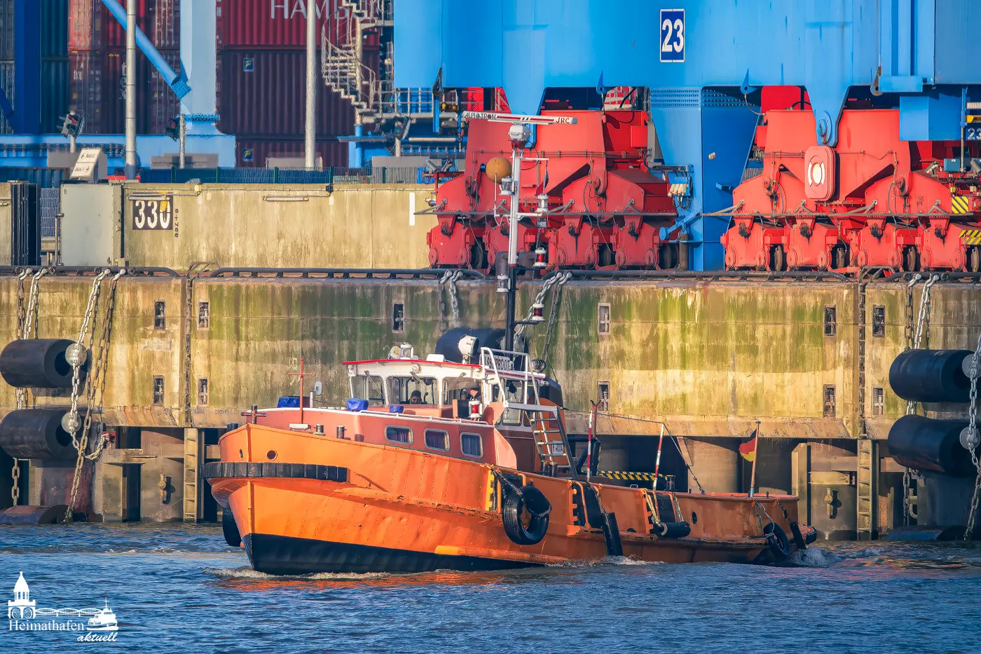 Gelbes Wasserboot liegt am Kai vor einem riesigen Containerterminal in Hamburg.