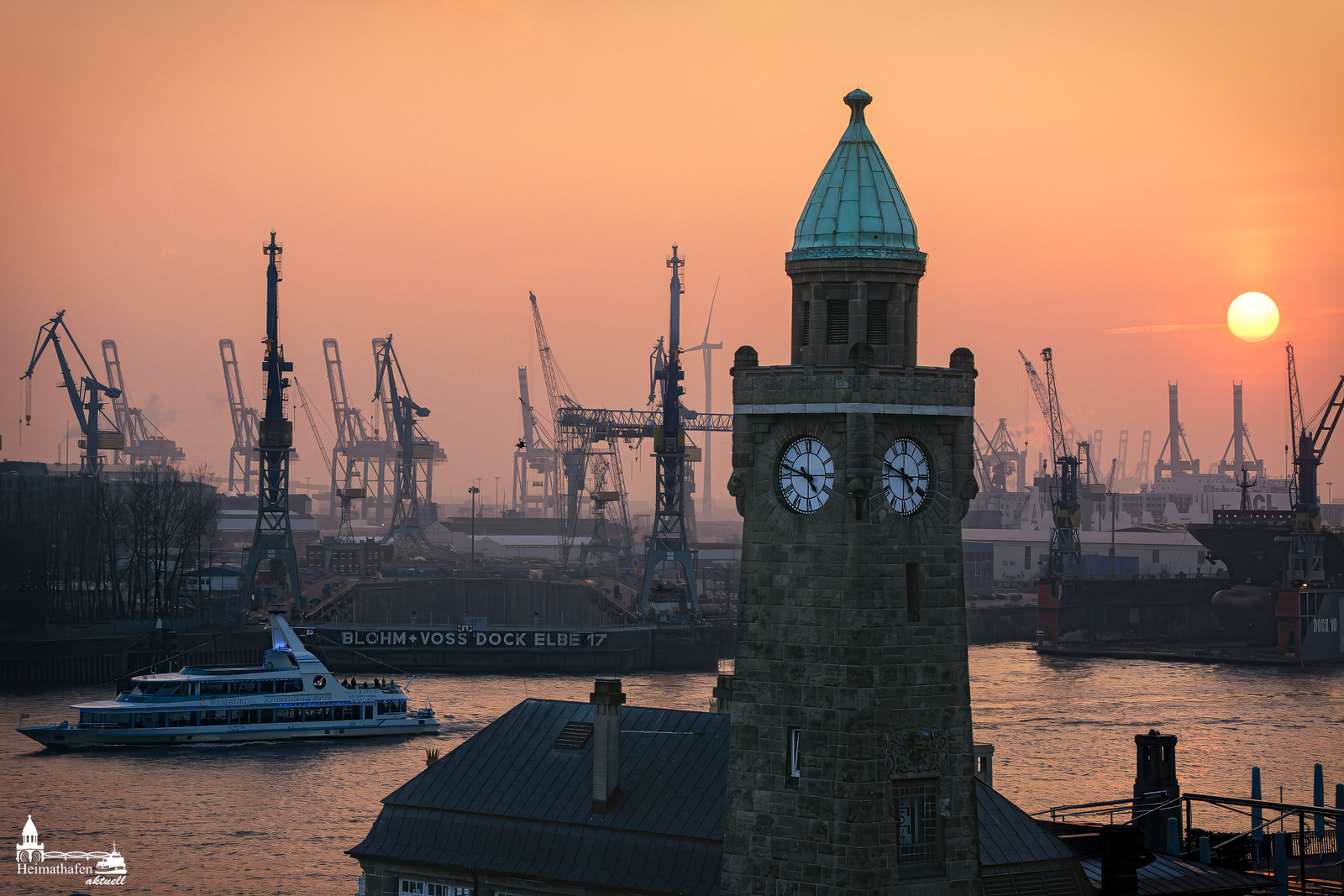 Pegelturm der Hamburger Landungsbrücken bei Sonnenuntergang mit Blick auf Blohm+Voss und Hafenkräne.