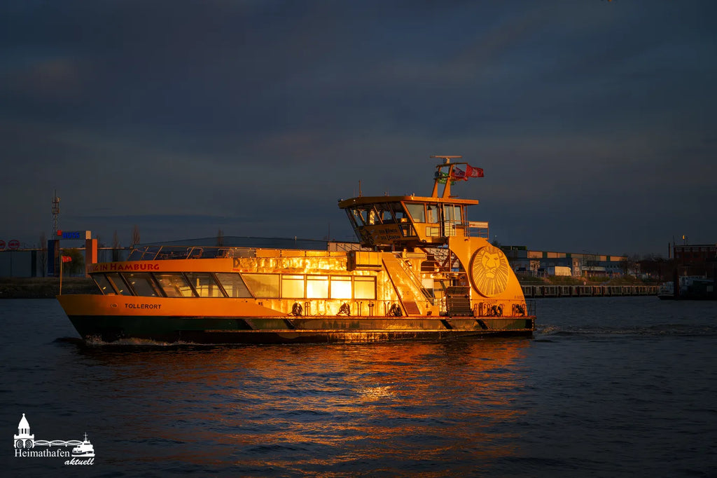 Hafenfähre Tollerort bei Sonnenuntergang in Hamburg, golden angestrahlt auf der Elbe mit dunklem Himmel im Hintergrund.
